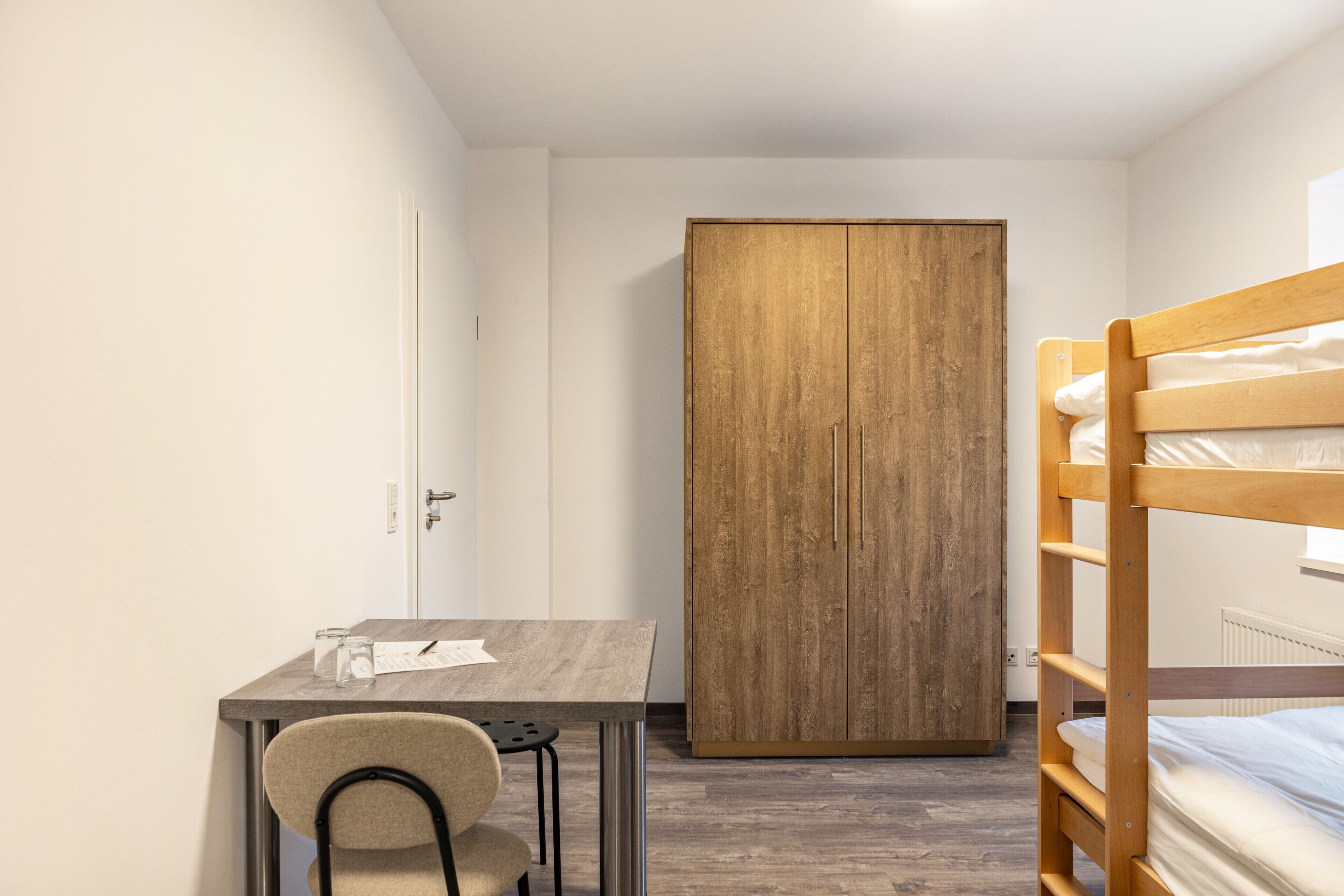 Un dormitorio con literas, un armario de madera, un escritorio con silla y un radiador.