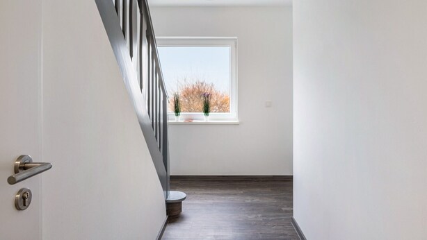 A hallway with a wooden floor, a white door with a silver handle, a window with a view of trees, and a white ceiling. - Haus Fuldablick 'Room 7' with Shared Garden and Wi-Fi (Rotenburg an der Fulda)