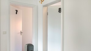A hallway with doors numbered 7 and 8, a grey chair, and a white wall. - Haus Fuldablick 'Room 7' with Shared Garden and Wi-Fi (Rotenburg an der Fulda)