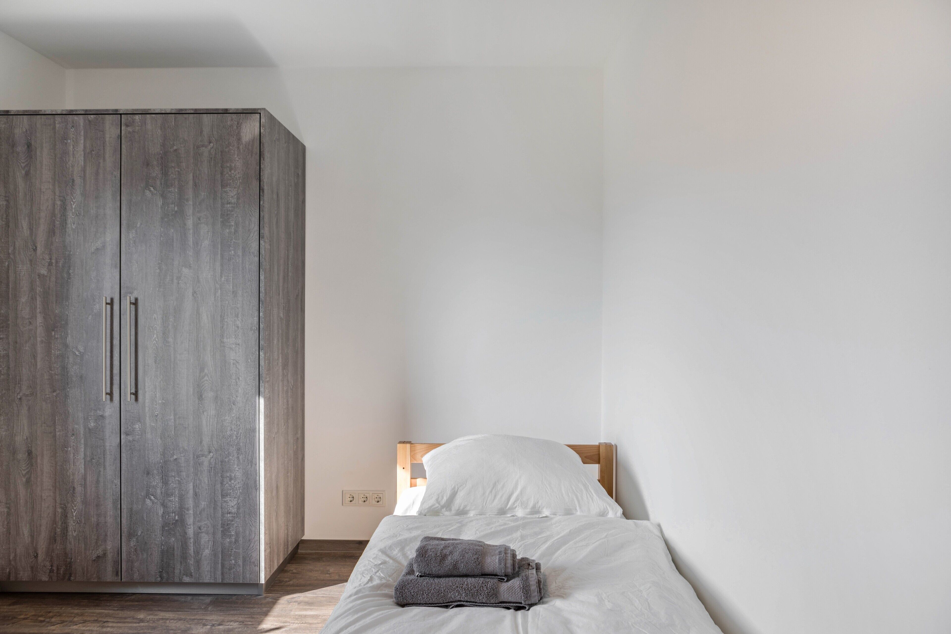 A bedroom with a bed, a wardrobe, and a wall socket.