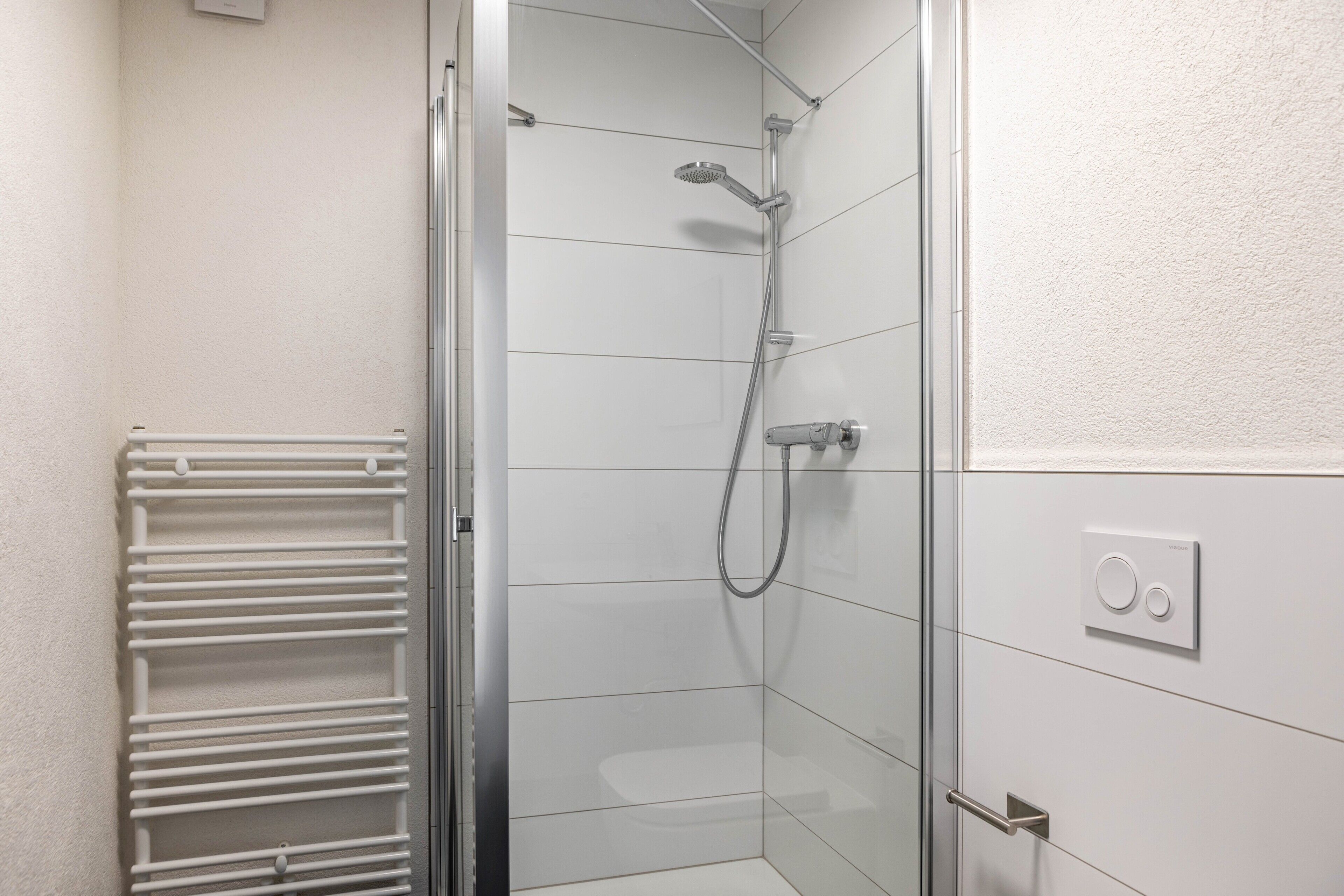 A glass-enclosed shower with a handheld showerhead, a towel rack, and a control panel on the wall.