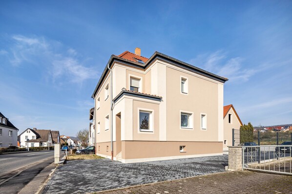 A multi-story residential building with a paved driveway and a gated parking area.