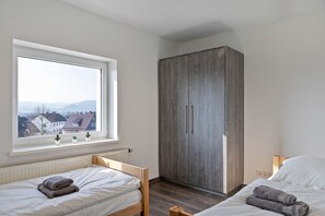 A bedroom with two beds, a wardrobe, a window with a view of houses, and a radiator.