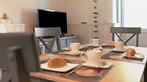Una mesa de comedor con una taza de café, un pastel y un televisor al fondo.