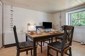 Un comedor con una mesa de madera, cuatro sillas, un televisor y una ventana con vistas a árboles.