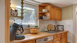 Una cocina con armarios de madera, una cafetera, un lavabo y una ventana con cortinas.