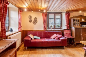 Une pièce chaleureuse avec un canapé en cuir rouge, un plancher en bois, un radiateur, un meuble en bois et des rideaux à carreaux rouges.