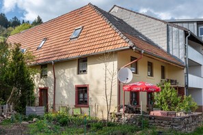 Un bâtiment à deux étages, doté d’un toit recouvert de tuiles rouges, d’une antenne parabolique et d’un parasol rouge.