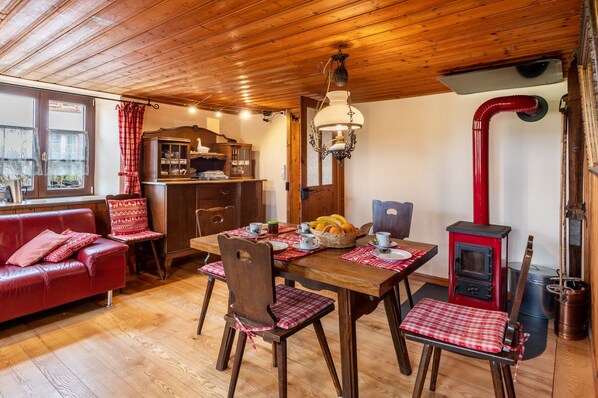 Une pièce chaleureuse avec un plafond en bois, une table à manger avec des chaises, un canapé rouge et un poêle à bois.
