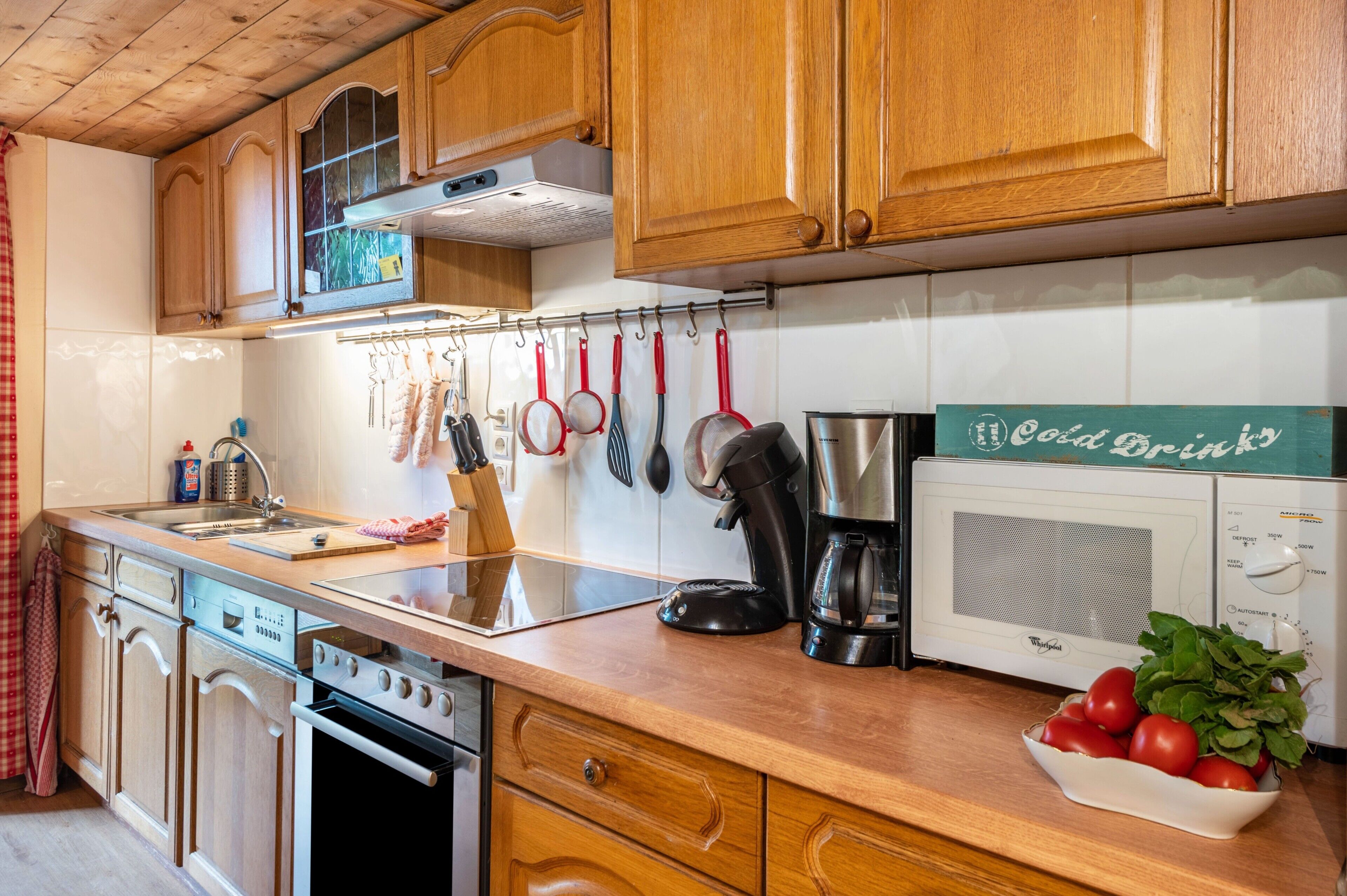 A kitchen with wooden cabinets, a stainless steel sink, a coffee maker, and a bowl of tomatoes.