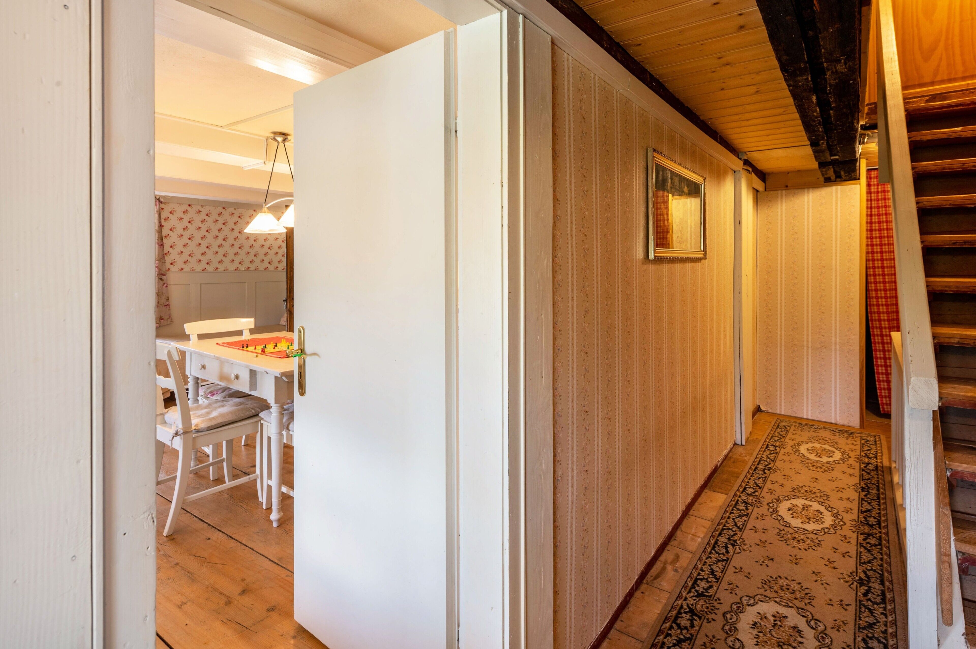 Un couloir avec un tapis à motifs, un escalier en bois et un coin repas comprenant une table et des chaises.