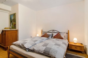 A bedroom with a bed, bedside lamps, a wooden nightstand, a wooden dresser, and a painting on the wall.