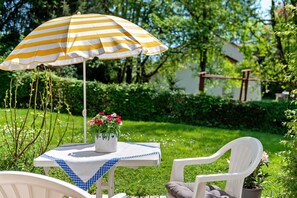 A garden setting with a table, chairs, a striped umbrella, and a potted plant with flowers. - Apartment 'Zizi' with Mountain View, Private Terrace and Wi-Fi (Stockach)