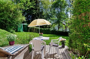 A wooden deck with a table and chairs, surrounded by greenery and a house in the background. - Apartment 'Zizi' with Mountain View, Private Terrace and Wi-Fi (Stockach)