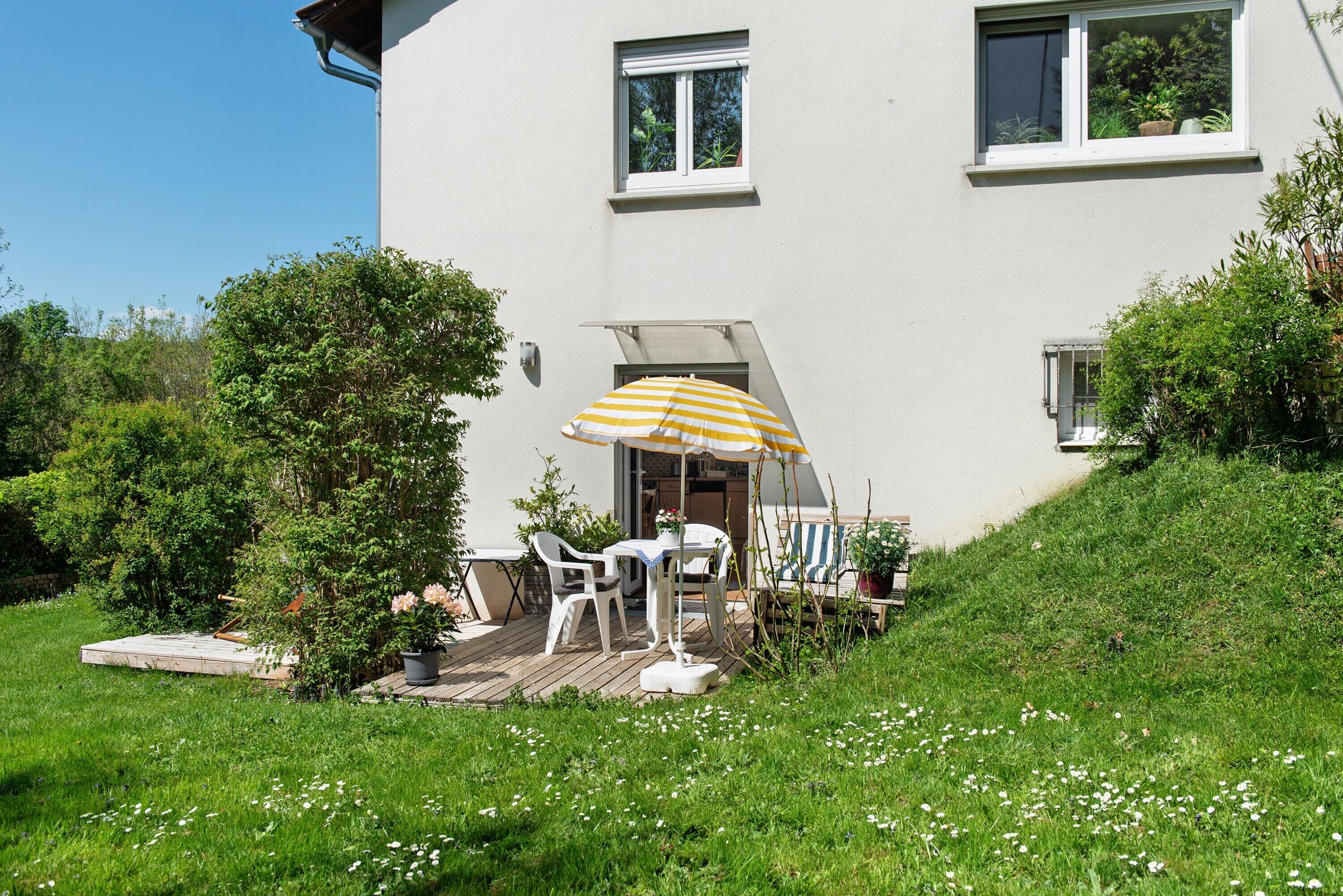 Una casa con un patio, mobiliario exterior y un paraguas amarillo.