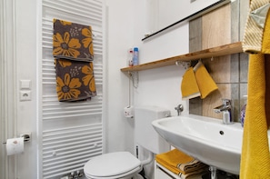 A bathroom with a toilet, sink, towel rack, and a wooden shelf.
