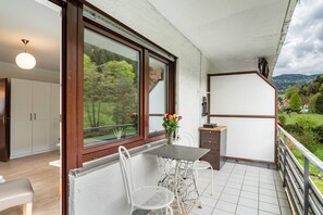 Un balcon avec une table et des chaises, un vase rempli de fleurs et une vue sur la verdure et les collines.