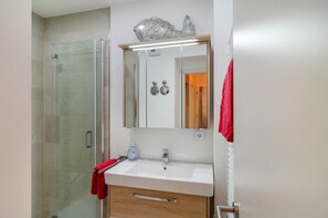 Un bagno con cabina doccia in vetro, un lavandino bianco con specchio sopra e un asciugamano rosso appeso al muro.