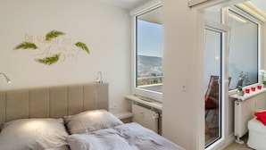 A bedroom with a bed, a window, a radiator, and a small table with a plant and candles. - Apartment 'Wolke8' with Private Sauna, Stunning Mountain Views, Balcony, Wi-Fi, Parking (Goslar-Hahnenklee)