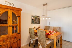 Un'area pranzo con un tavolo in legno, sedie in vimini e un mobile con vetrine.