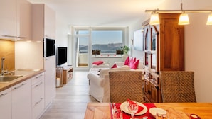 A modern kitchen with a TV, dining area with a table set for two, and a balcony with a view. - Apartment 'Wolke8' with Private Sauna, Stunning Mountain Views, Balcony, Wi-Fi, Parking (Goslar-Hahnenklee)
