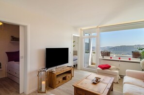 Un salon équipé d’un téléviseur, de meubles en bois, d’un canapé et offrant une vue sur un paysage montagneux grâce à de grandes fenêtres.