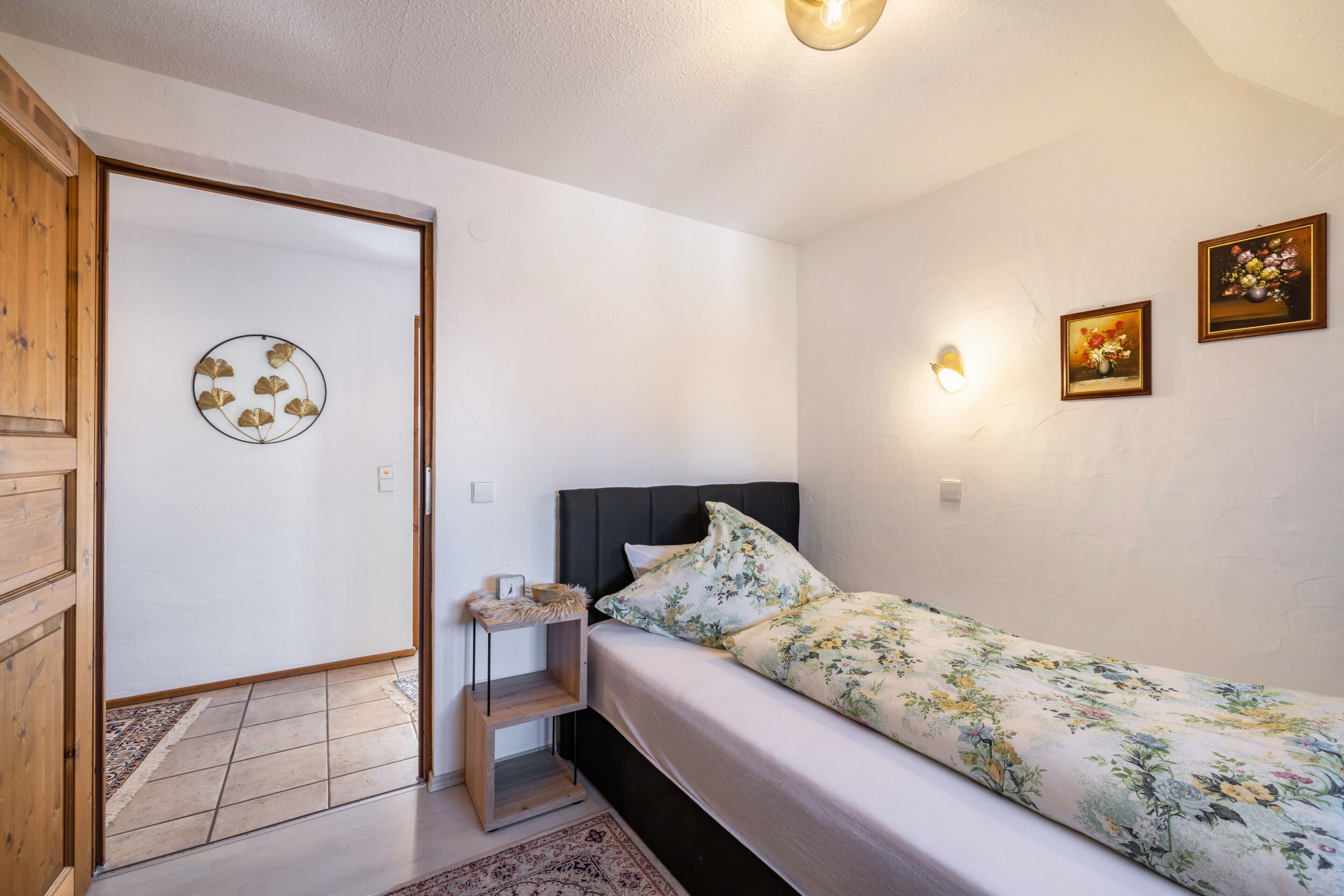Ein Schlafzimmer mit einem Bett, einem Nachttisch, einer Wandlampe und zwei gerahmten Bildern.