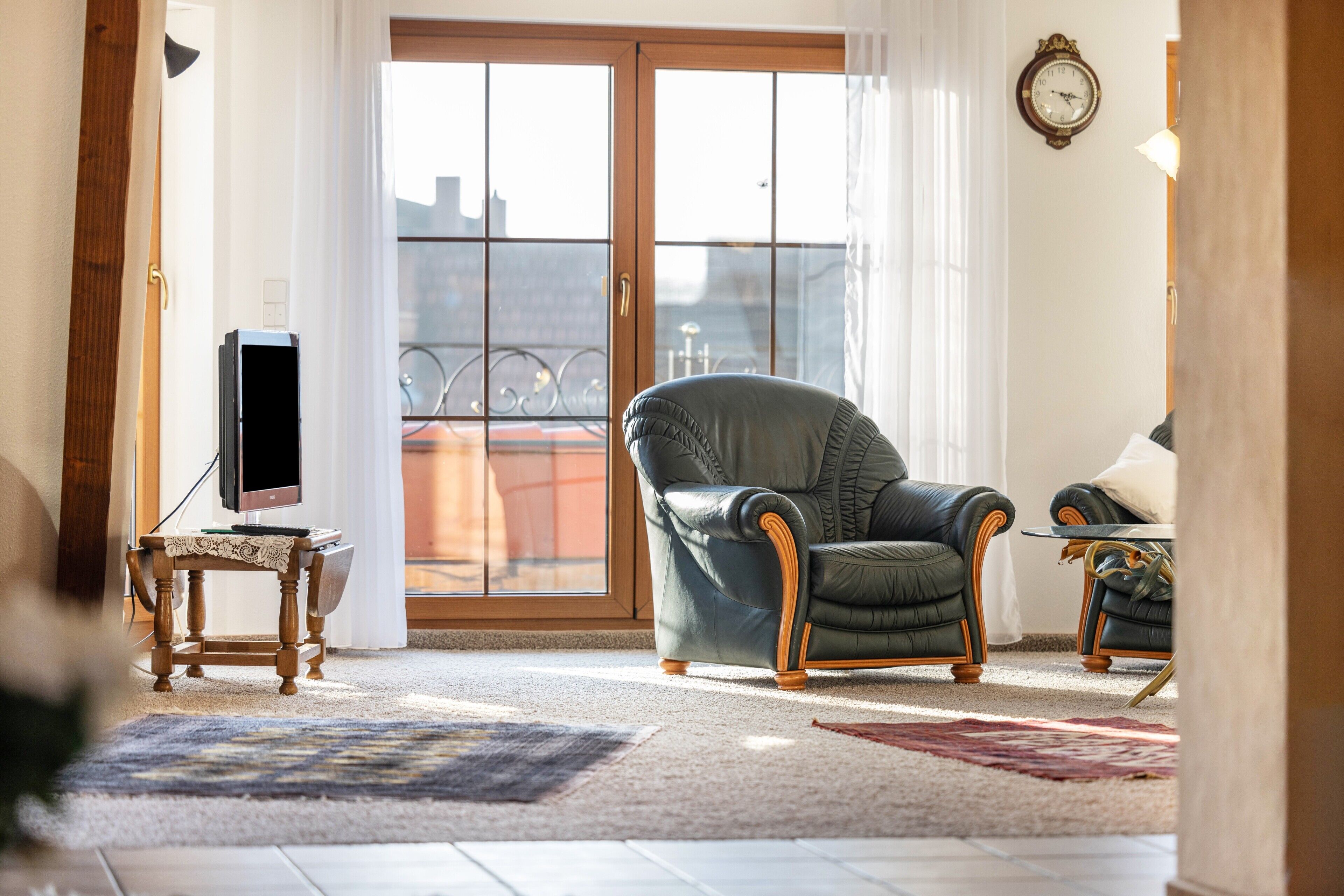 Un salon comprenant un fauteuil en cuir, une petite table avec une lampe, un téléviseur posé sur un meuble et une grande porte-fenêtre coulissante donnant sur un balcon.