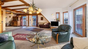 A spacious living room with a high ceiling, a glass coffee table, leather sofas, a fireplace, and large windows.