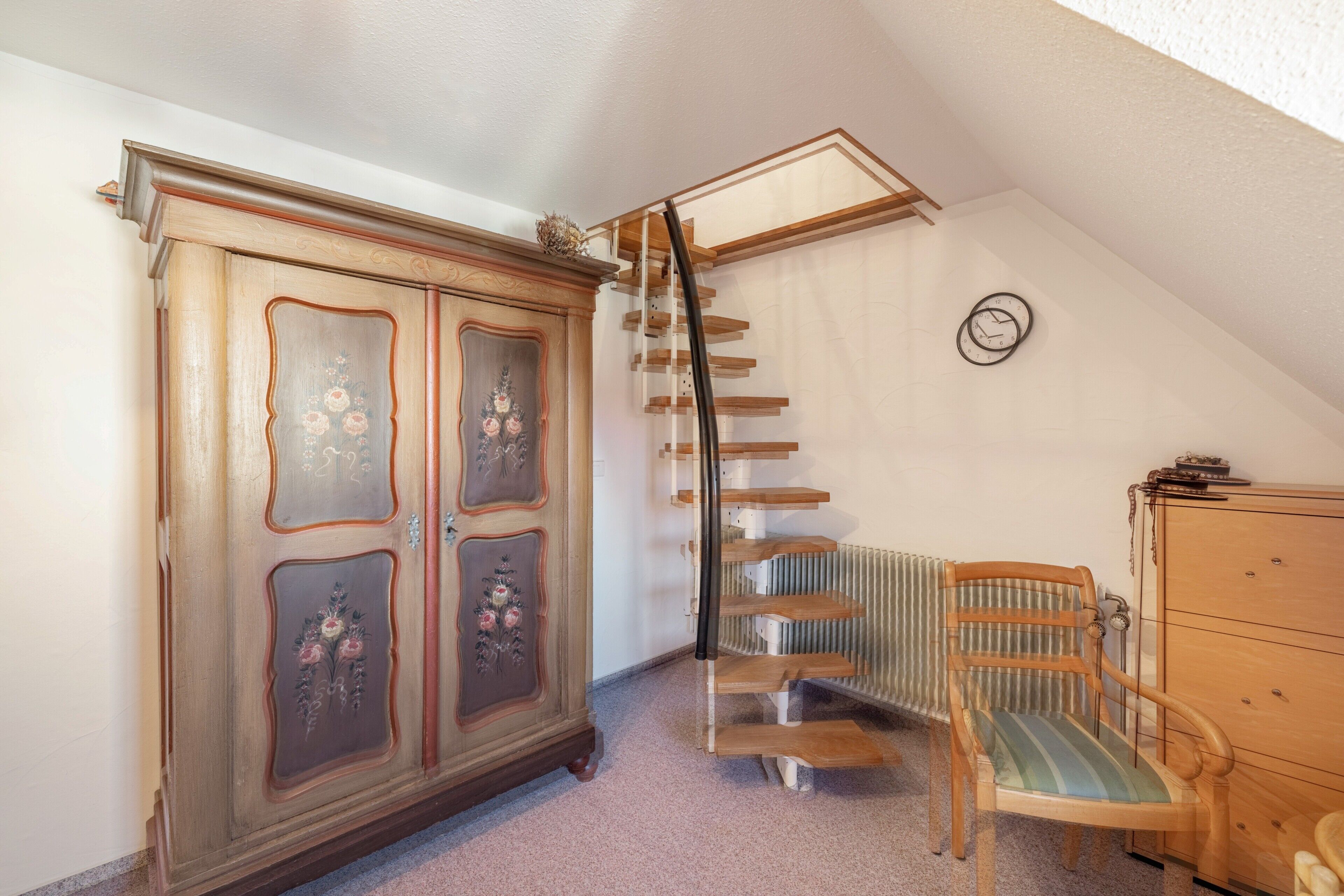 A room with a wooden wardrobe, a chair, a radiator, and a staircase.