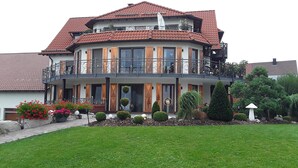 A two-story house with a balcony, a tiled roof, and a well-maintained garden.