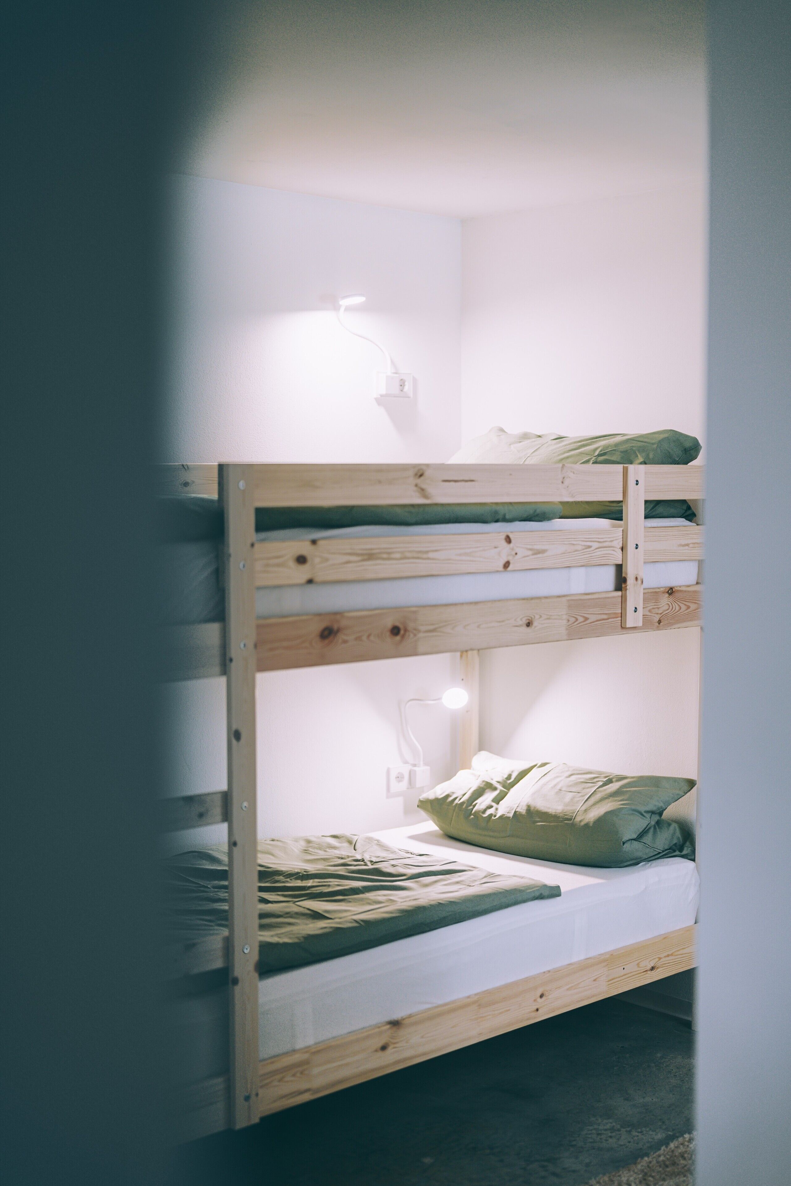 A bunk bed with a wooden frame, a white mattress, and a green pillow.