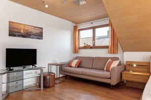 Una sala de estar moderna con un mueble bajo de vidrio para la televisión, un sofá, una mesita y un ventanal con cortinas.
