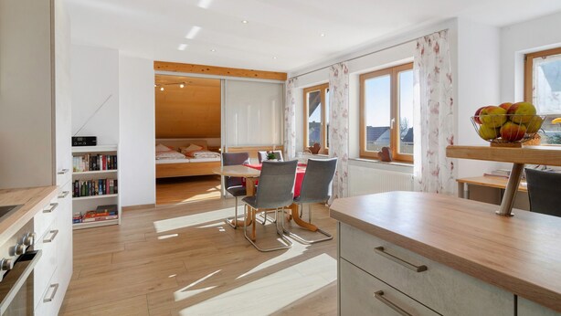 A modern room with a wooden floor, a dining area with chairs, a kitchen counter, and a bed with a wooden headboard. - Apartment 'Haus Am Ettenberg' with Balcony and Wi-Fi (Frickingen)