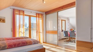 A bedroom with a bed, wooden ceiling, sliding glass doors to a balcony, and a dining area with chairs and a table. - Apartment 'Haus Am Ettenberg' with Balcony and Wi-Fi (Frickingen)