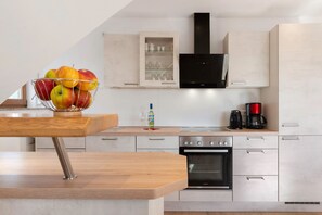 Una cocina moderna con una mesa de madera, un frutero, una cafetera y electrodomésticos de acero inoxidable.