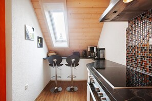 Een keuken met een houten plafond, een raam, twee barkrukken, een fornuis en een betegelde spatwand.