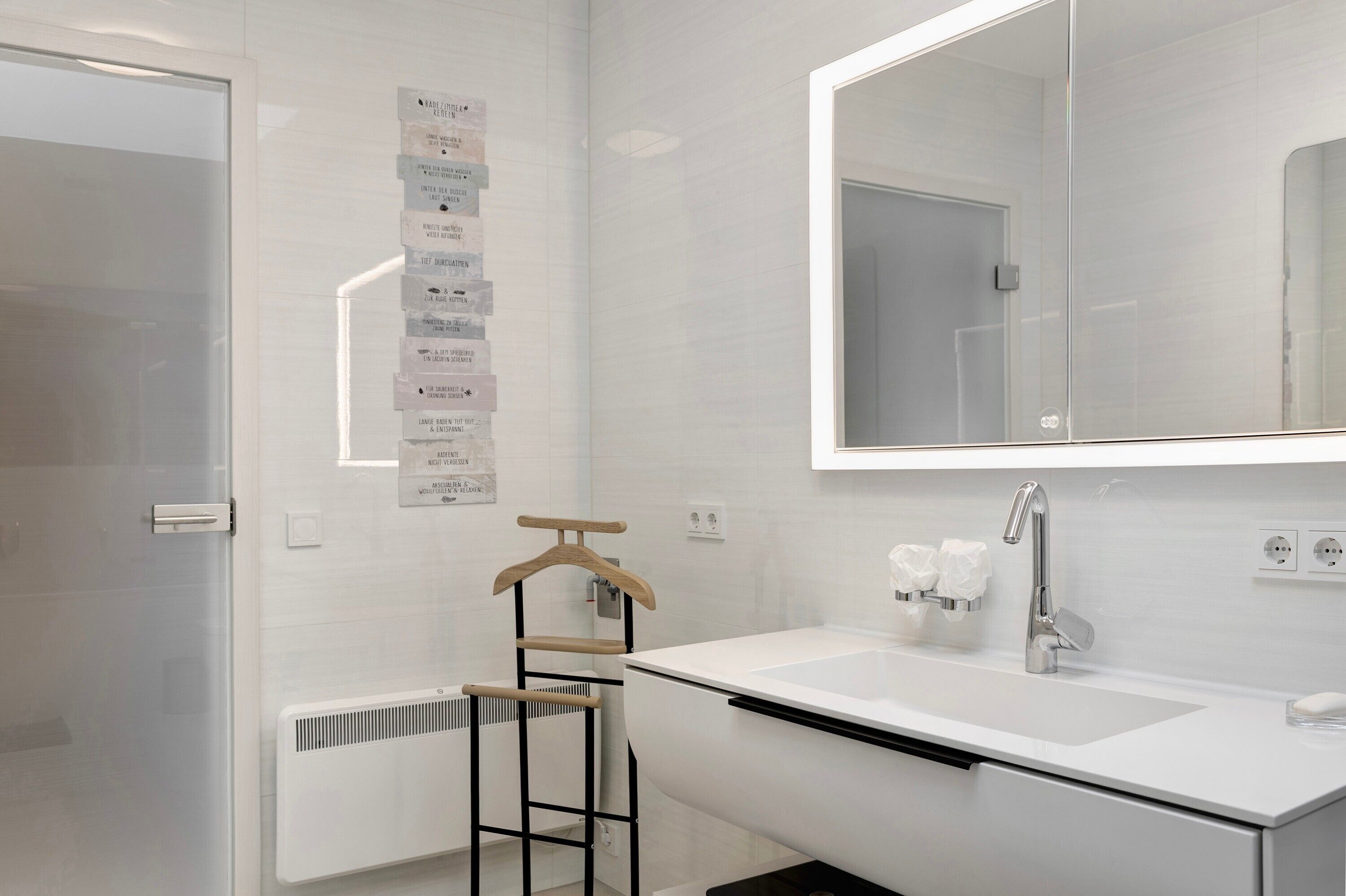 A modern bathroom with a large mirror, white sink, and towel rack.