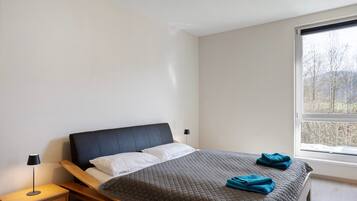 A bedroom with a bed, bedside table, lamp, and a window with a view.