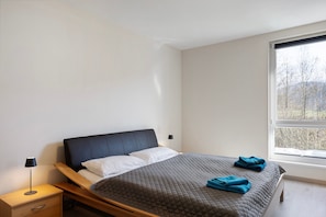 Une chambre à coucher avec un lit, une table de chevet, une lampe et une fenêtre donnant sur un beau paysage.