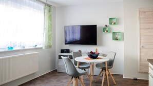 A modern living room with a flat-screen TV, grey chairs, a round table, and a window with sheer curtains. - Apartment '2' with Shared Terrace, Private Garden and Wi-Fi (Großräschen)