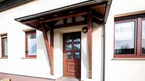 A building with a brown door, a covered porch, and two windows with curtains. - Apartment '2' with Shared Terrace, Private Garden and Wi-Fi (Großräschen)