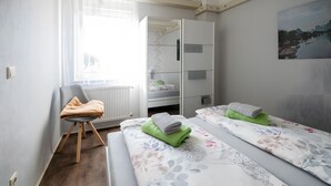 A bedroom with two beds, a chair, a radiator, and a window with curtains. - Apartment '2' with Shared Terrace, Private Garden and Wi-Fi (Großräschen)