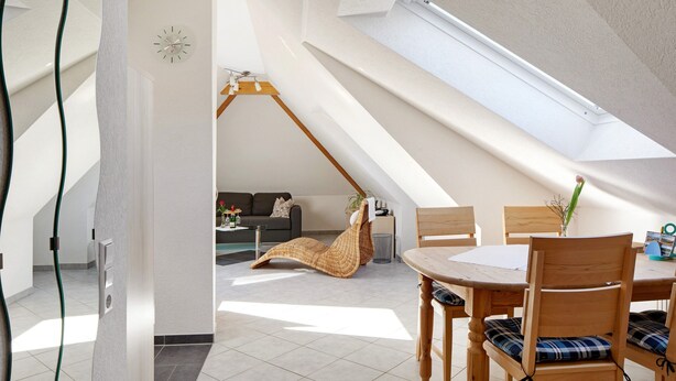 A modern interior with a dining area, a loft-style room, and a visible skylight.