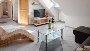 A modern loft with a glass coffee table, a sofa, a TV, and a skylight.