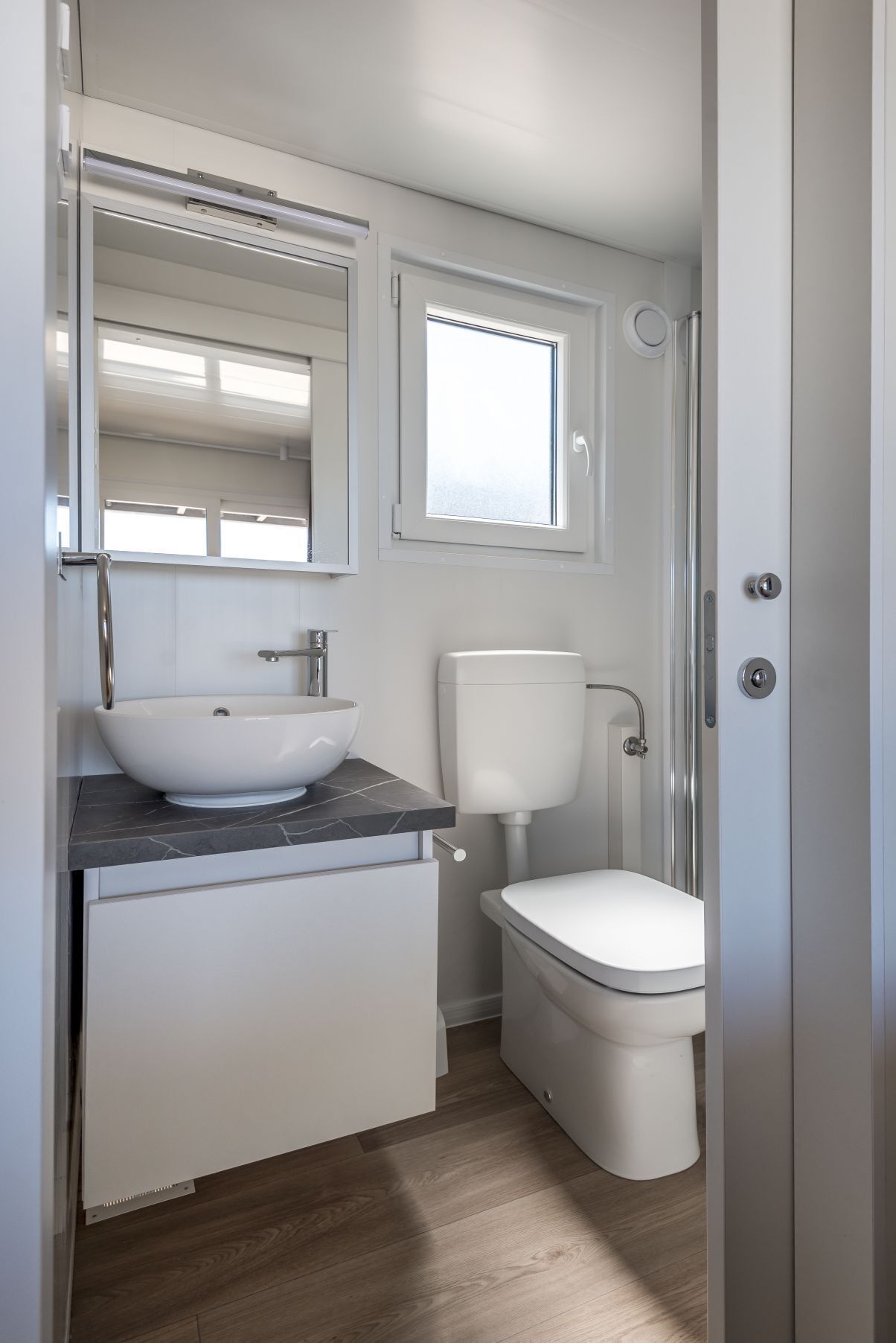 A compact bathroom with a vessel sink, toilet, and a window above the toilet.