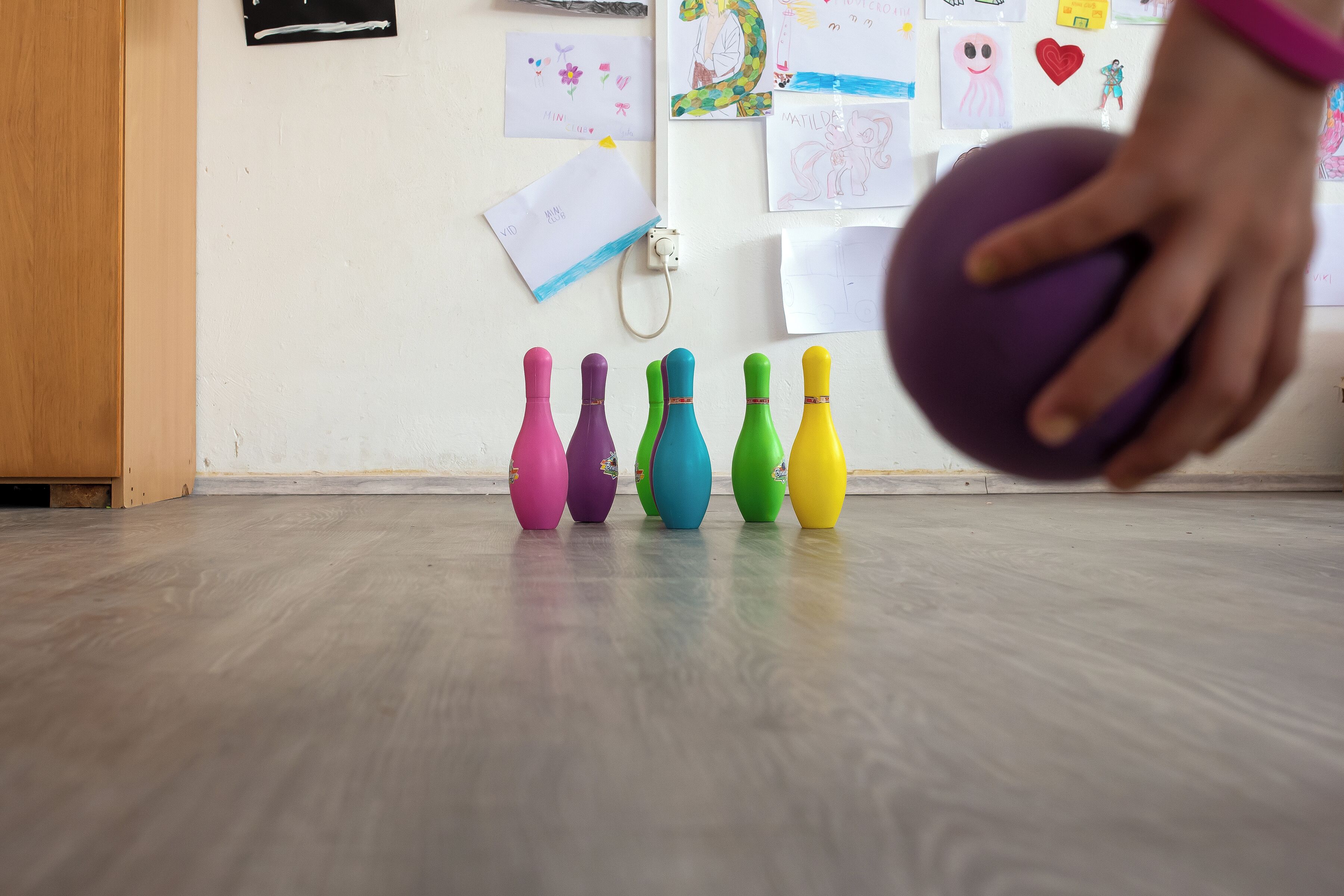 Eine Kegelbahn mit bunten Kegeln und einem violetten Bowlingball.