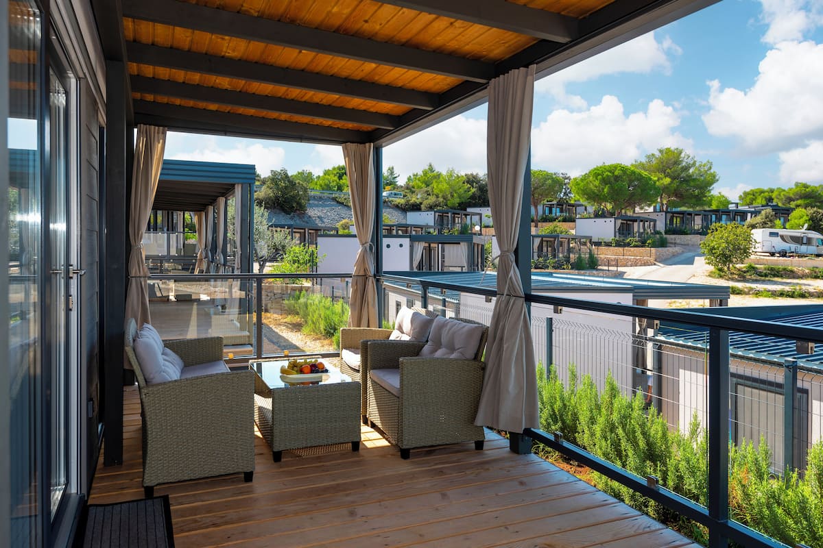 A covered outdoor seating area with wicker furniture and a table with fruit, overlooking a caravan park.