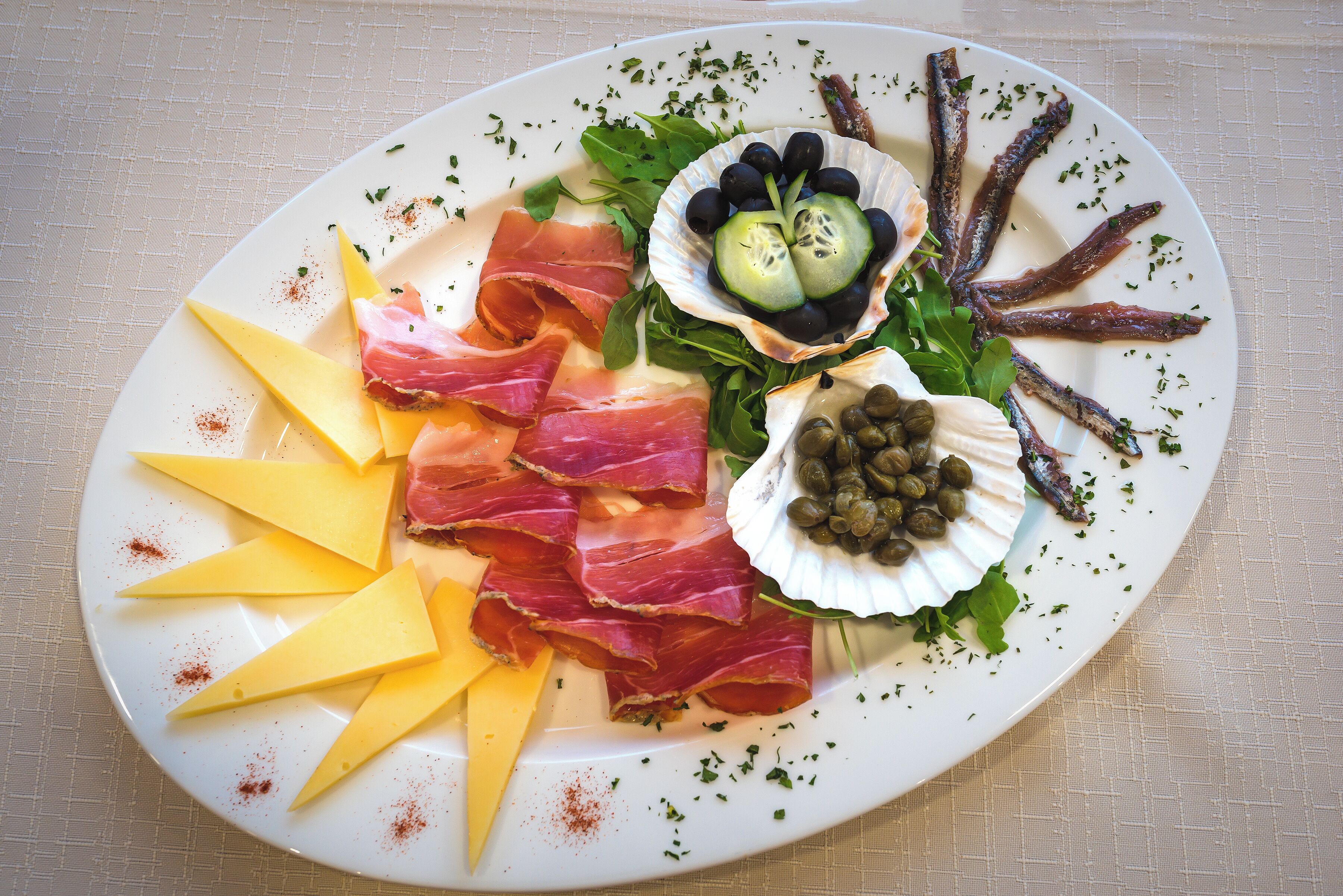 Un piatto con diversi assaggi tra cui formaggio, salumi, olive e capperi.