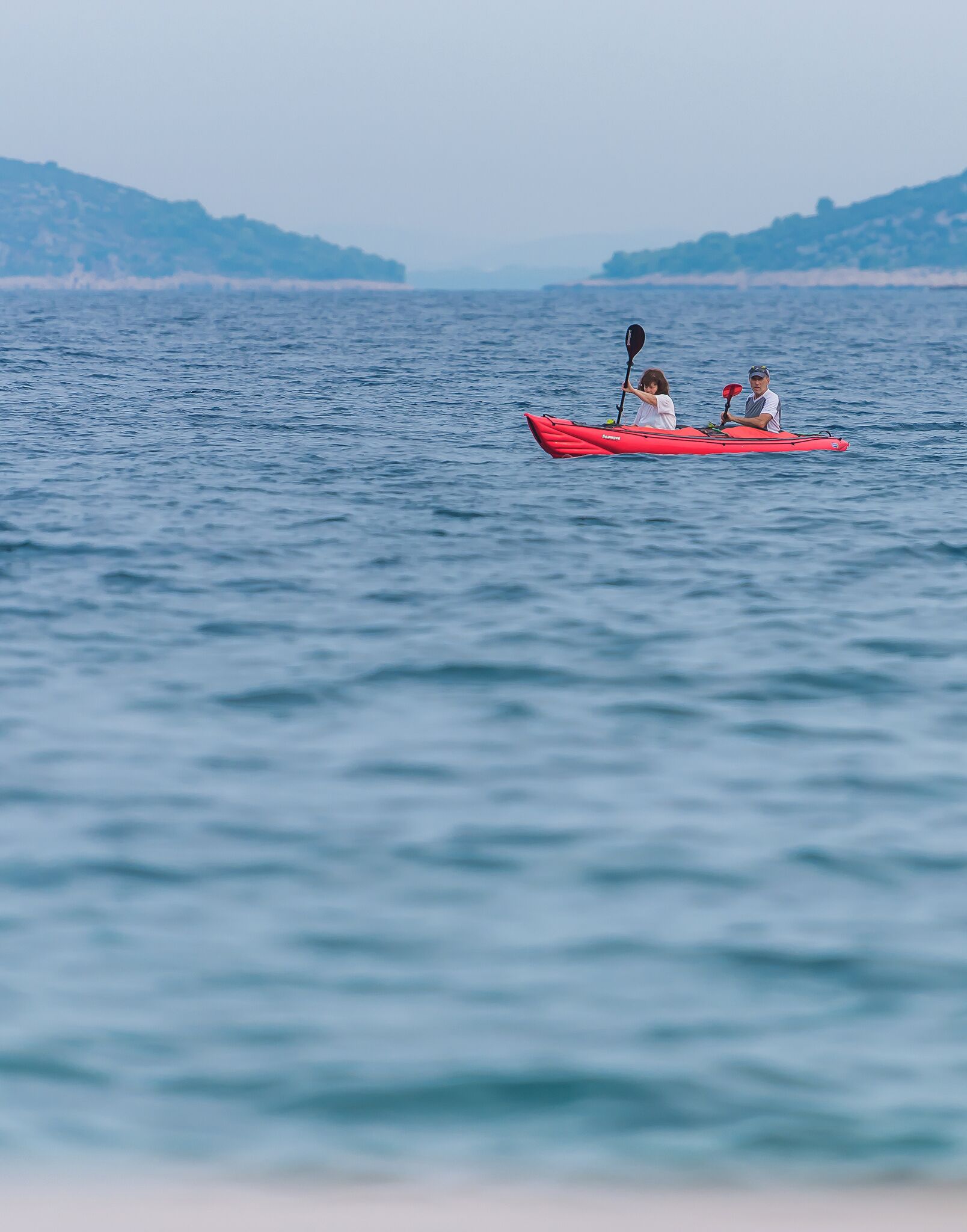 A red kayak on calm water with a distant shoreline.